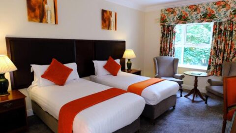 Elegant twin room with cosy beds, vibrant decor, bright window view, and inviting armchairs for a relaxing stay.