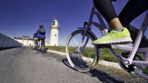 Guests cycling towards lighthouse on scenic path, enjoying outdoor adventure and beautiful sea views.