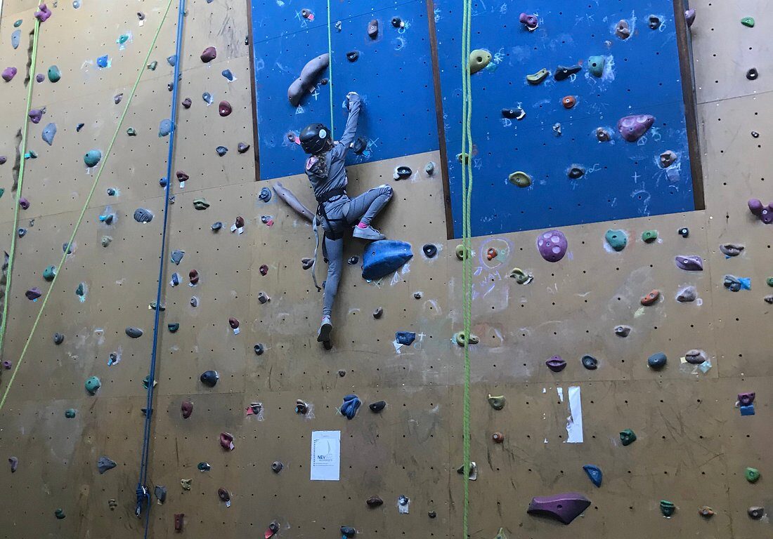 Guest rock climbing indoors at hotel gym, colourful holds, safety mats, and ropes, ideal for fitness and adventure.