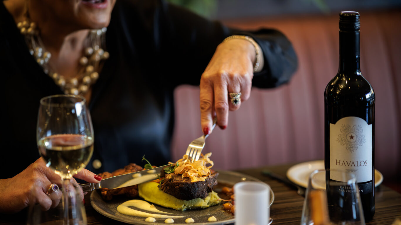 Guest enjoying gourmet steak dinner with wine in elegant hotel restaurant, featuring ambient candle lighting and plush seating.