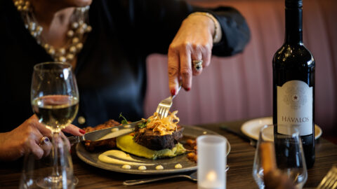 Guest enjoying gourmet steak dinner with wine in elegant hotel restaurant, featuring ambient candle lighting and plush seating.