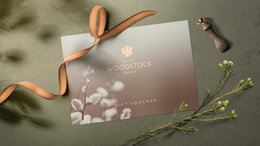 Elegant gift voucher with luxurious ribbon, floral accents, and Hotel Woodstock branding on a sophisticated backdrop.