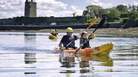Guests kayaking on calm waters with historic castle backdrop, enjoying outdoor adventures and stunning scenery.
