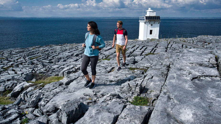 Couple exploring scenic coastal cliffs near a lighthouse with stunning sea views, perfect for a romantic getaway.