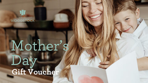 Smiling mother and child embrace in cosy kitchen, holding a card. Celebrate Mother's Day at upscale Hotel Woodstock.
