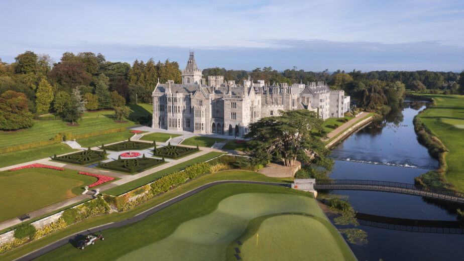 A large stone castle with manicured gardens, a river, and a golf course, viewed from above on a clear day.