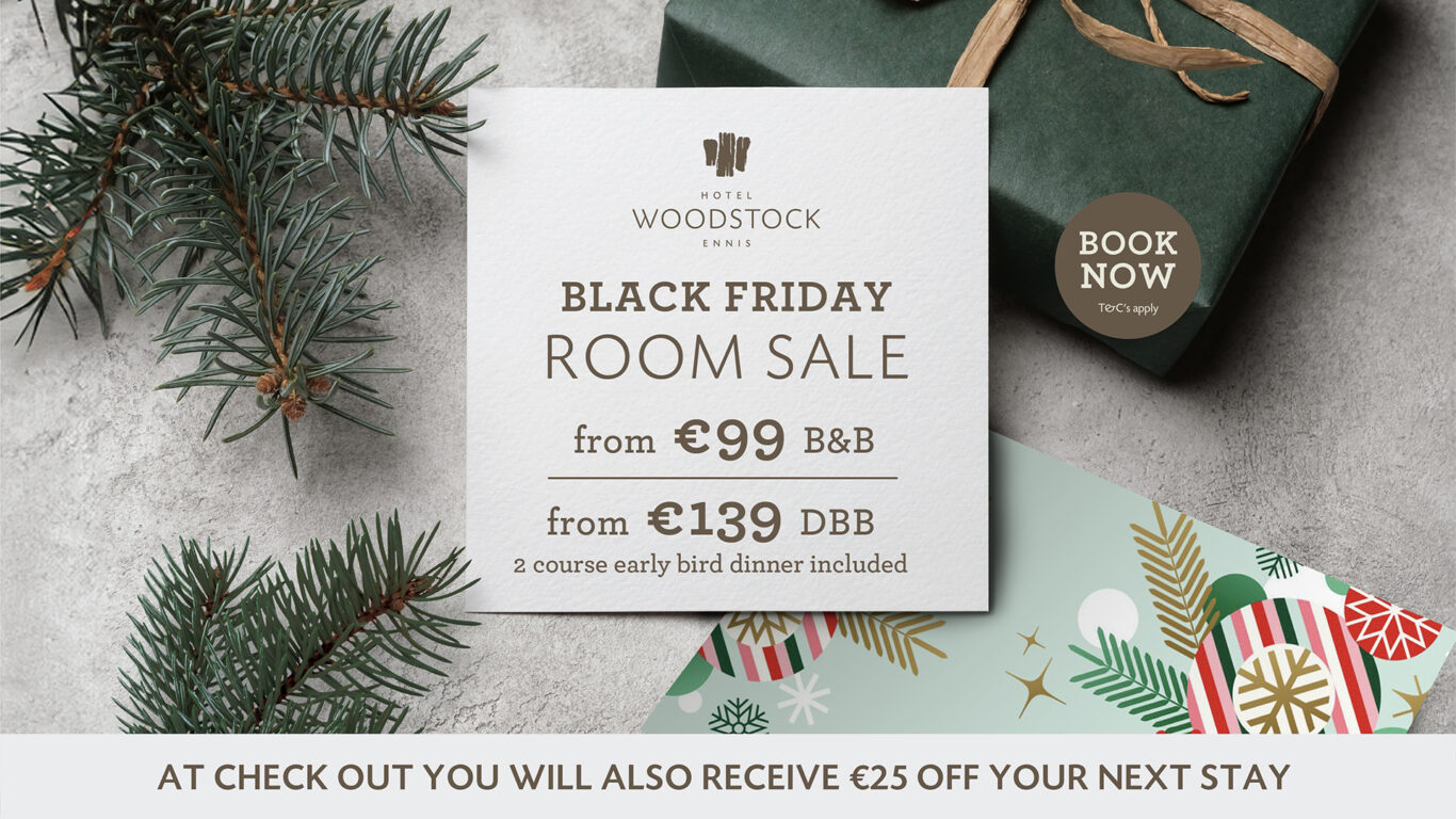 A Black Friday room sale sign from Hotel Woodstock Ennis is displayed on a table with a wrapped gift, pine branches, and greeting cards. Offer details and a promotion for €25 off are shown.