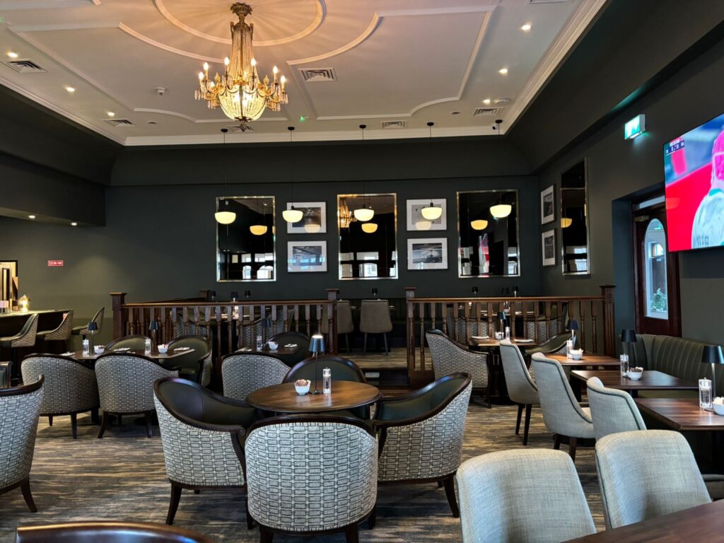 Elegant hotel restaurant with chandeliers, comfortable seating, modern decor, and a large TV for guest enjoyment.