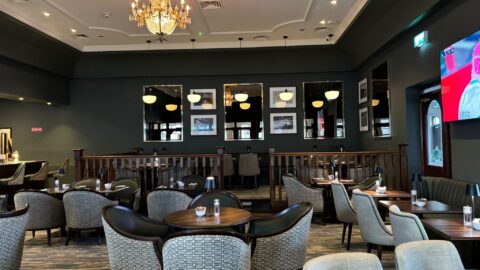 Elegant hotel restaurant with chandeliers, comfortable seating, modern decor, and a large TV for guest enjoyment.