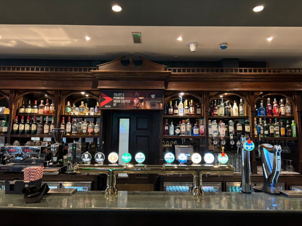 Elegant hotel bar with classic wood panelling, diverse spirits selection, taps for draught beers, and cosy lighting.