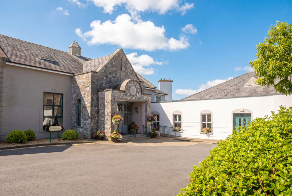 Charming stone hotel entrance with lush greenery and sunny skies, inviting guests to a serene, picturesque retreat.