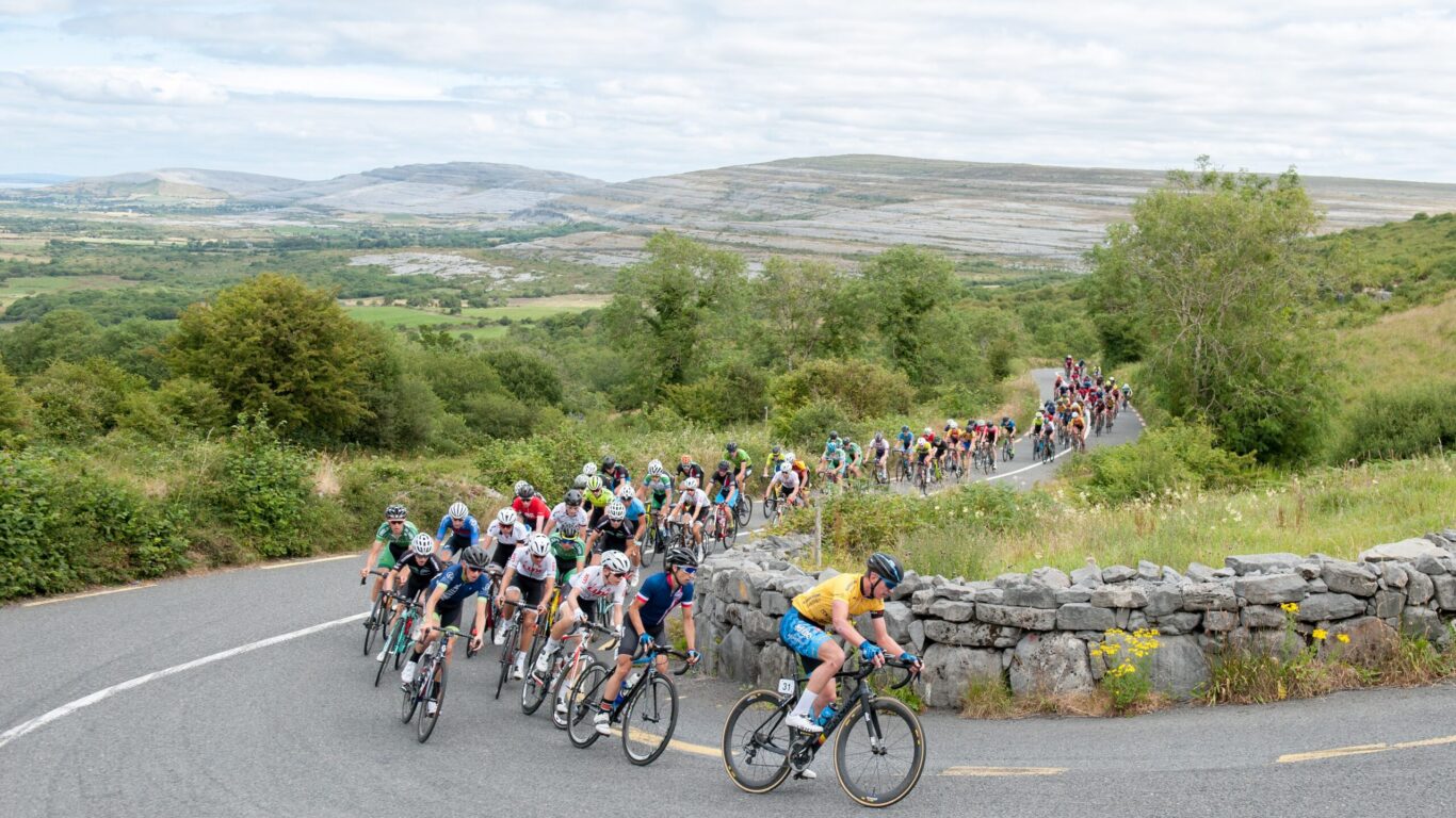 Cyclists race through scenic countryside with lush hills and stone walls, offering guests thrilling views of nature and sport.