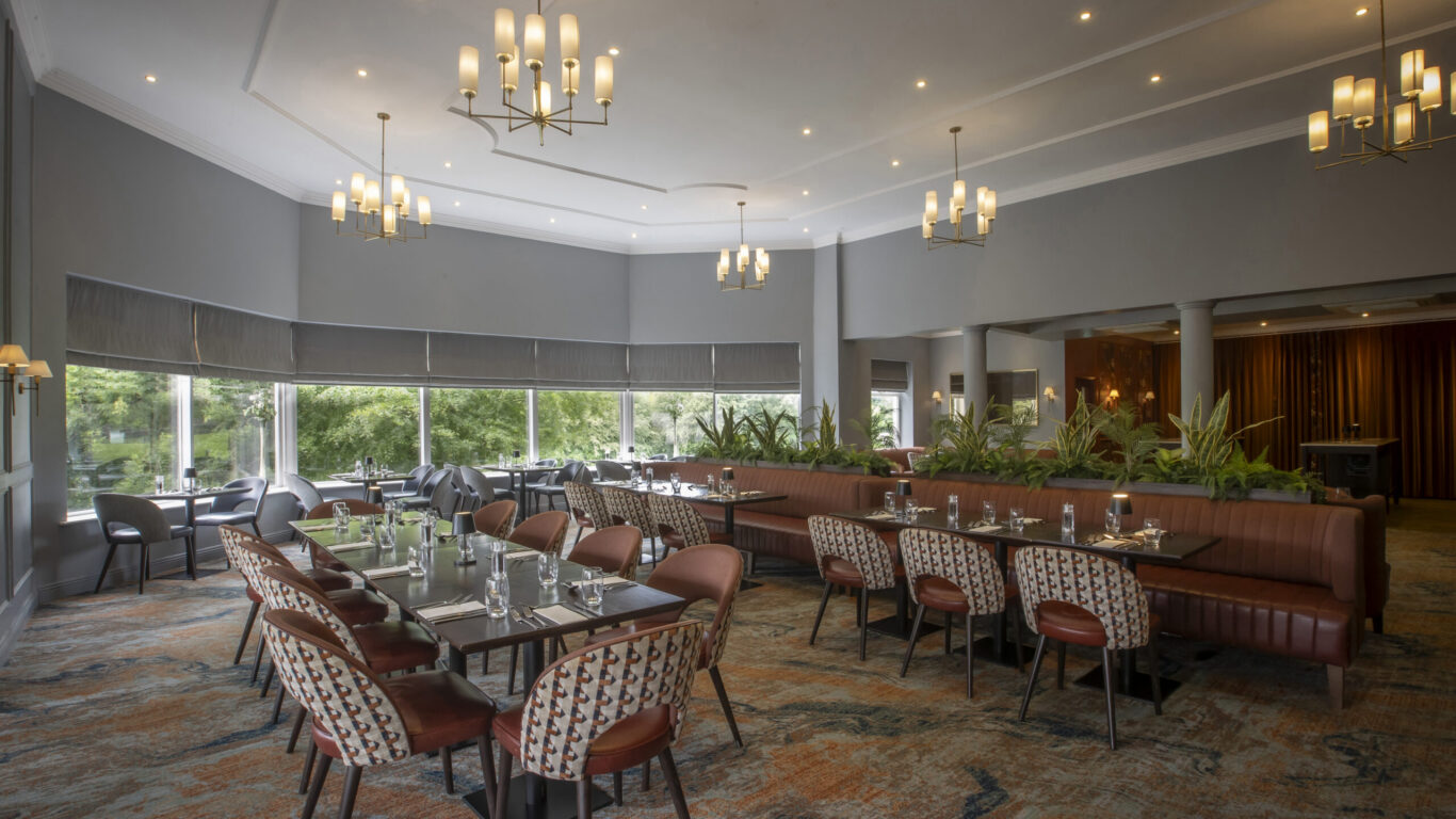 Spacious hotel dining room with modern d&eacute;cor, elegant lighting, large windows, and garden views. Perfect for relaxed meals.