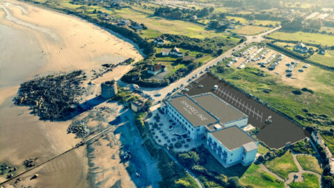 Aerial view of Shoreline Hotel beside a scenic beach, showcasing coastal beauty and ample parking for a relaxing getaway.